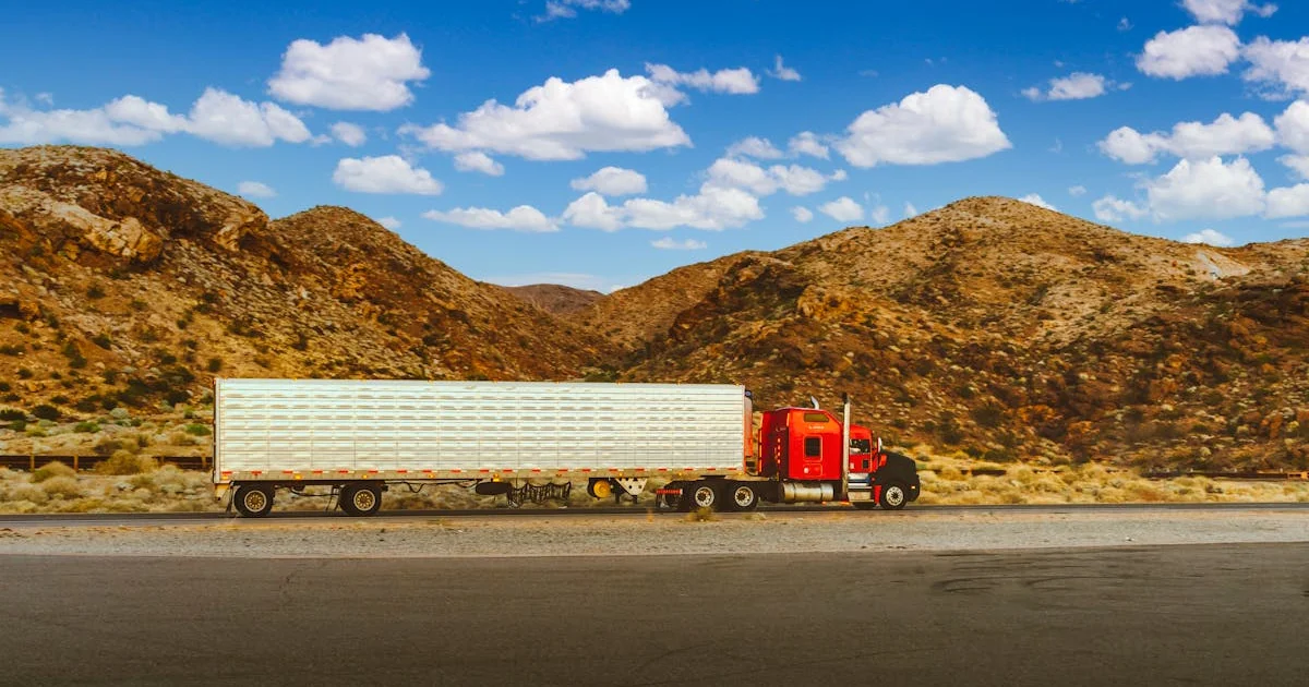 Red semi-truck on a desert highway with mountains and blue sky